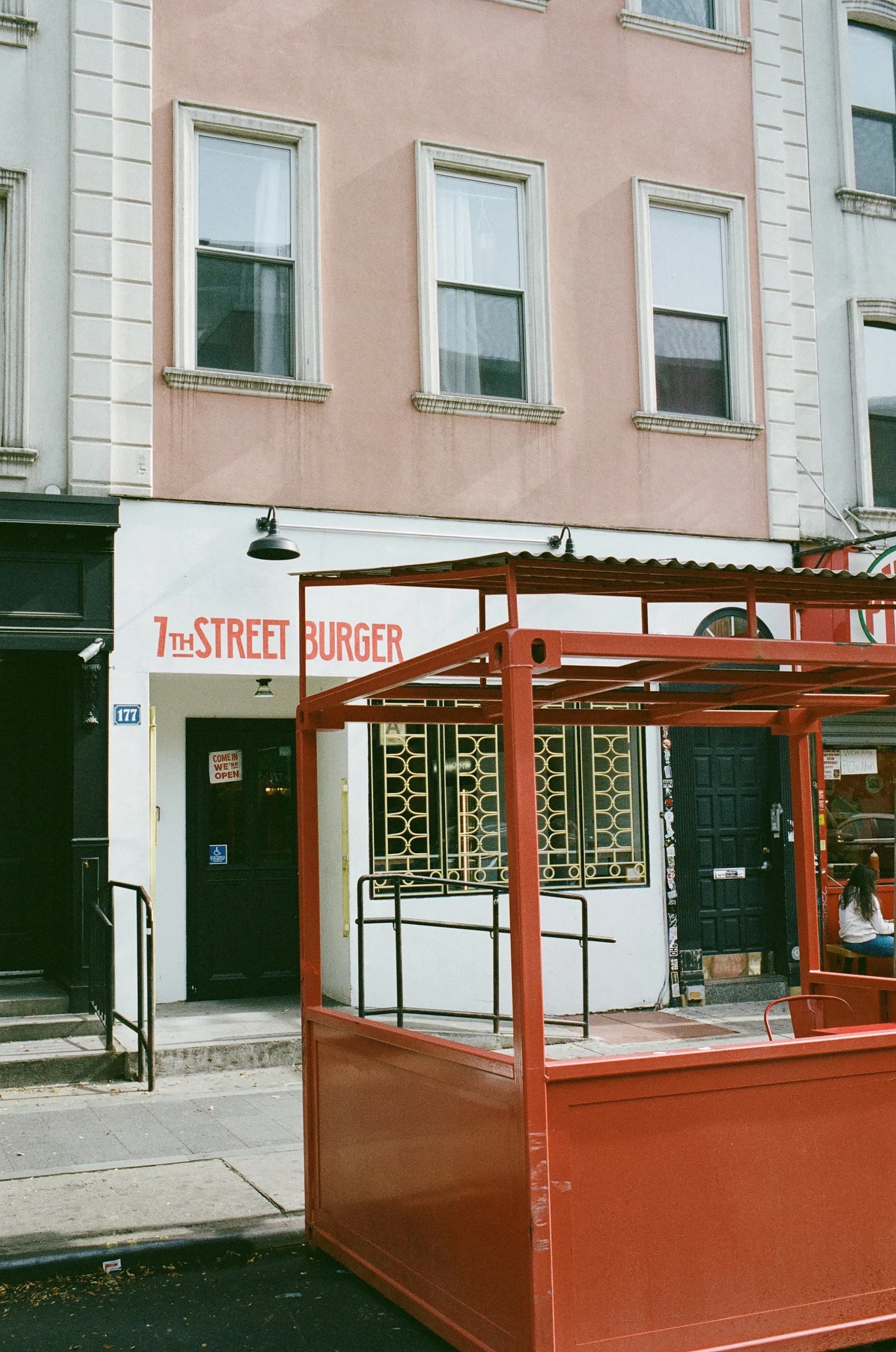Exterior shot of the Williamsburg 7th Street Burger. White building with green doors and gold accented windows 